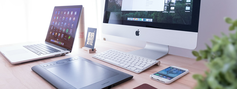 a laptop, desktop, tablet, and cell phone laying neatly on a wooden table, all showing different responsive websites.